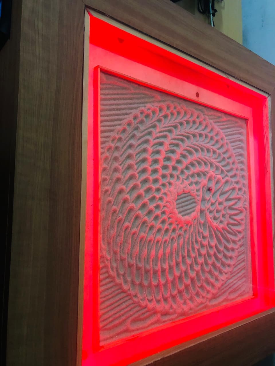 Vibrant red edge-lit sand vortex pattern inside wooden furniture bezel