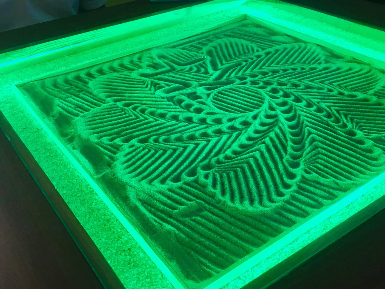 Kinetic Sand Mandala illuminated in green LED showing multi-layered geometric ripples